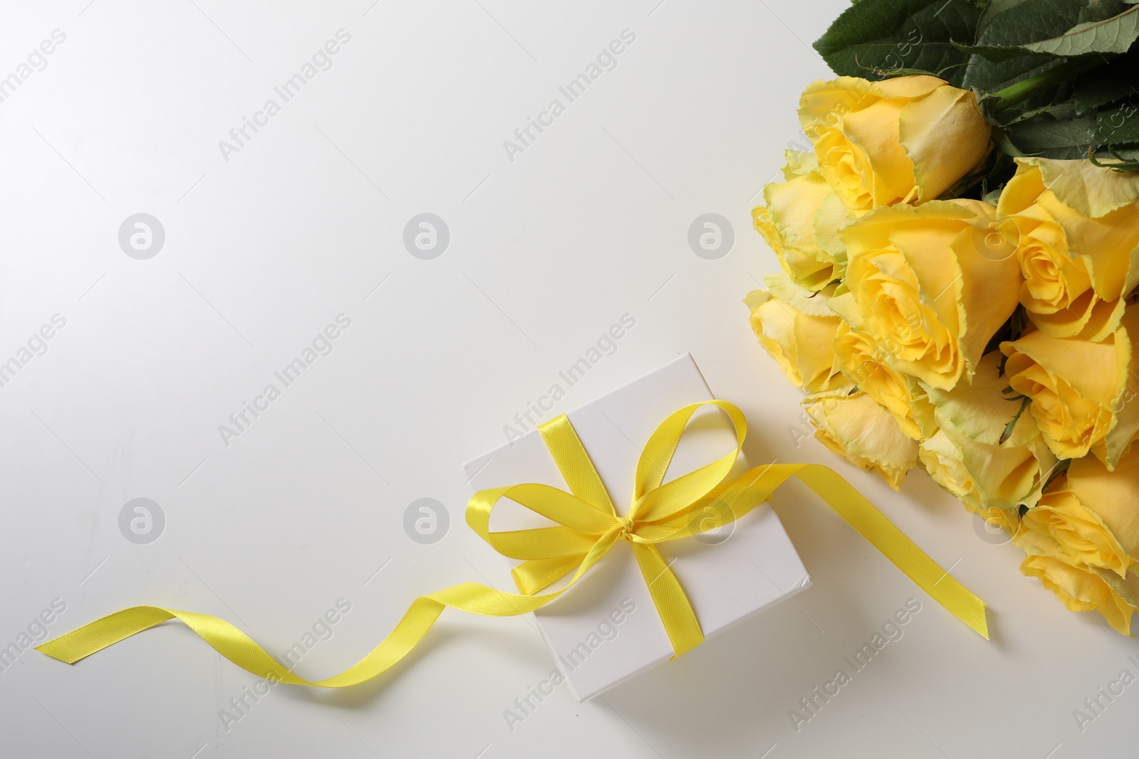 Photo of Beautiful bouquet of yellow roses and gift box on white background, flat lay. Space for text