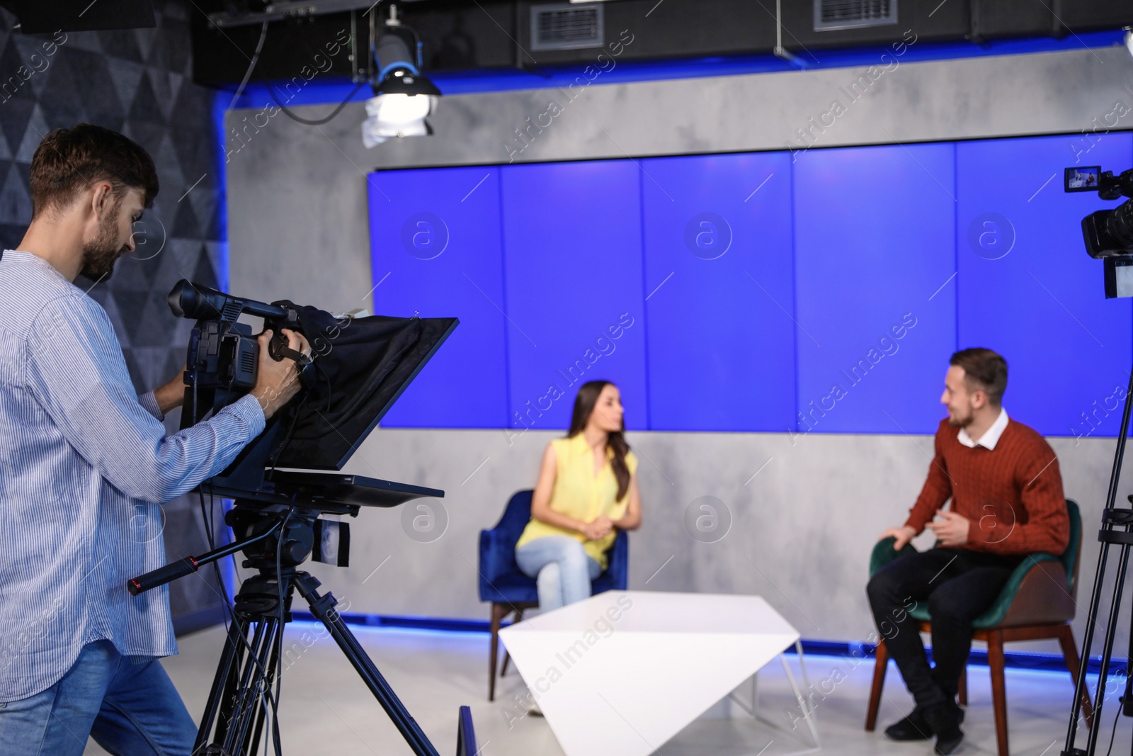 Photo of Presenters and video camera operator working in studio. News broadcasting