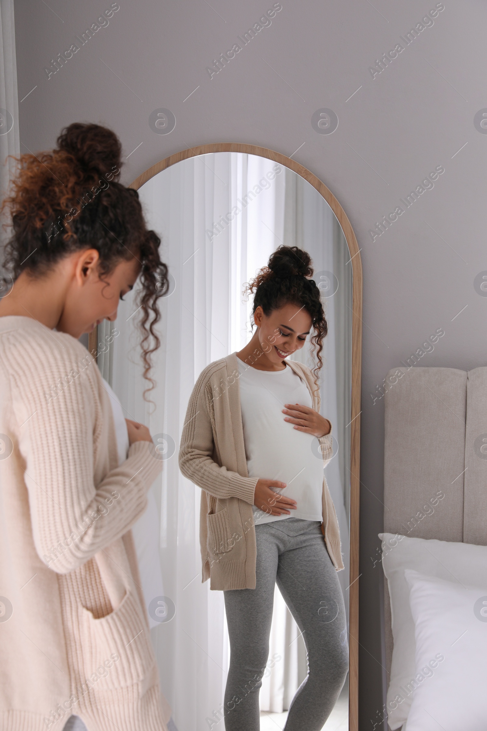 Photo of Pregnant young African-American woman near mirror at home