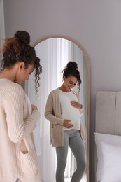 Pregnant young African-American woman near mirror at home