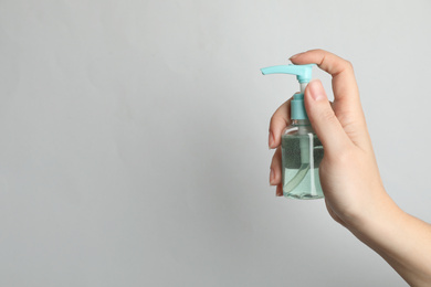 Photo of Woman holding antiseptic gel on light grey background, closeup. Space for text