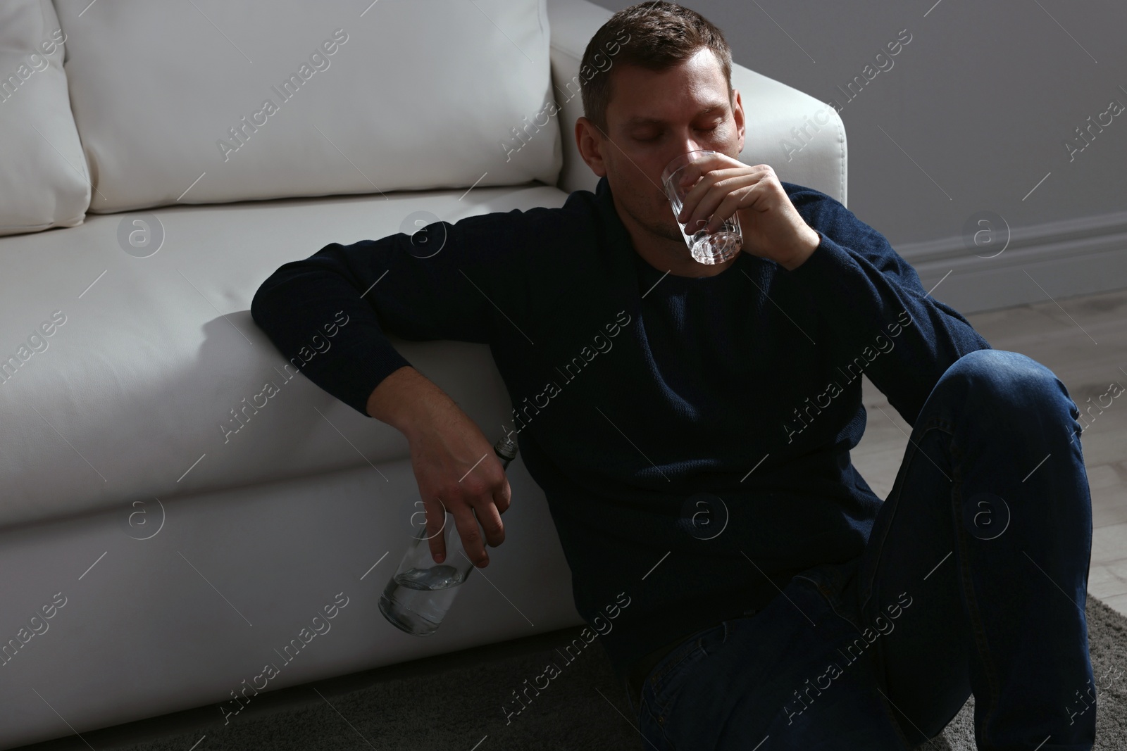 Photo of Addicted man drinking alcohol near sofa indoors