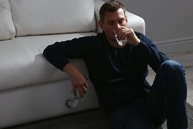 Photo of Addicted man drinking alcohol near sofa indoors
