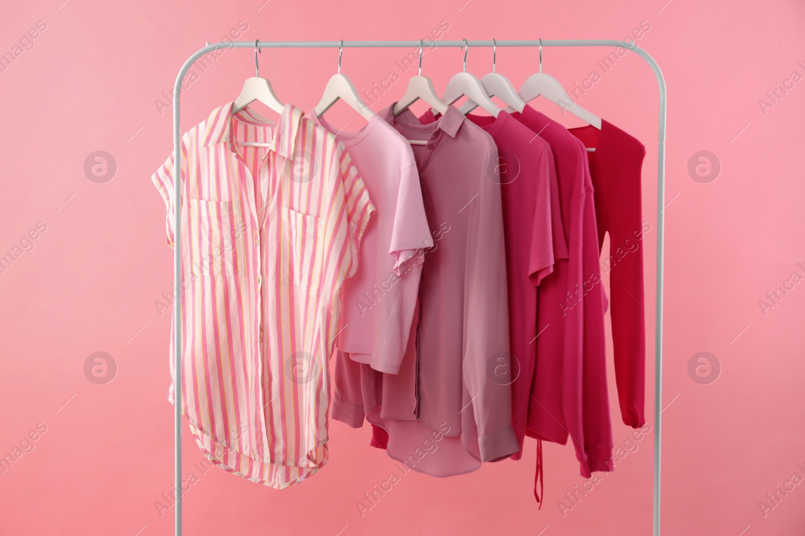 Photo of Rack with different stylish women's clothes on pink background