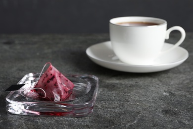 Photo of Saucer with used tea bag and cup of hot drink on grey table