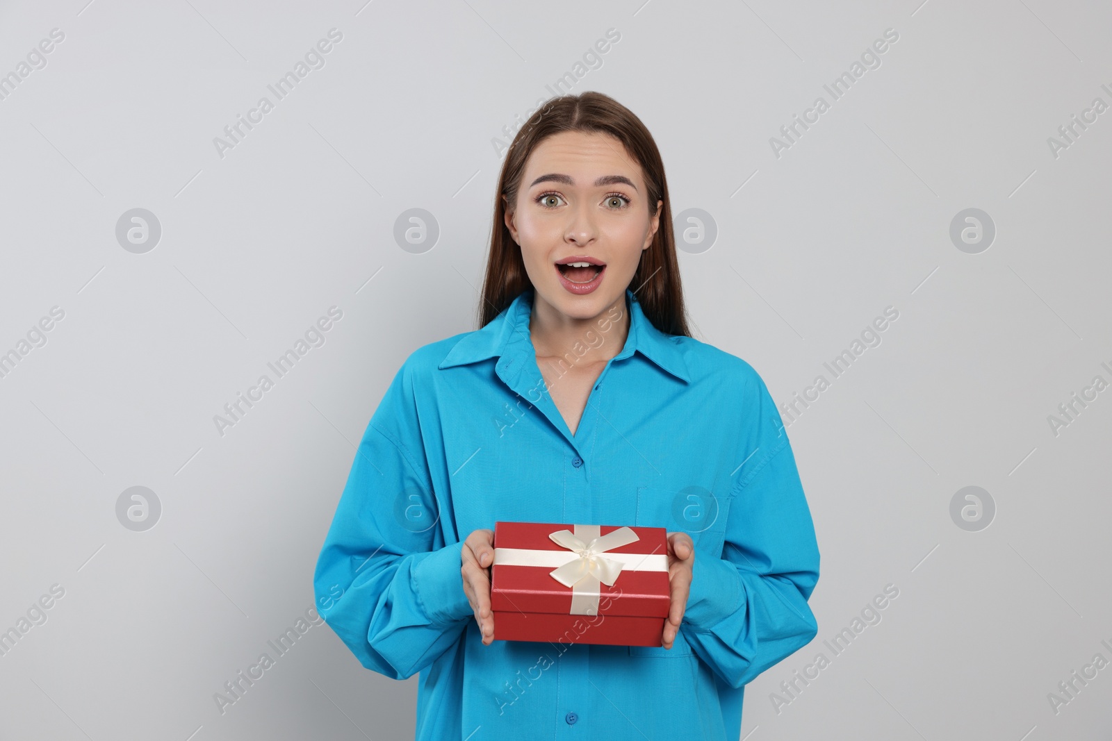 Photo of Portrait of emotional young woman with gift box on grey background