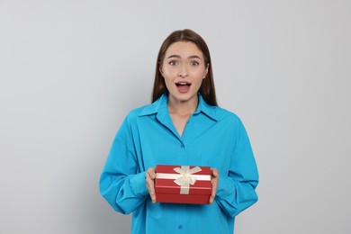 Portrait of emotional young woman with gift box on grey background