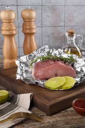 Aluminum foil with raw meat, rosemary, lime and spices on wooden table