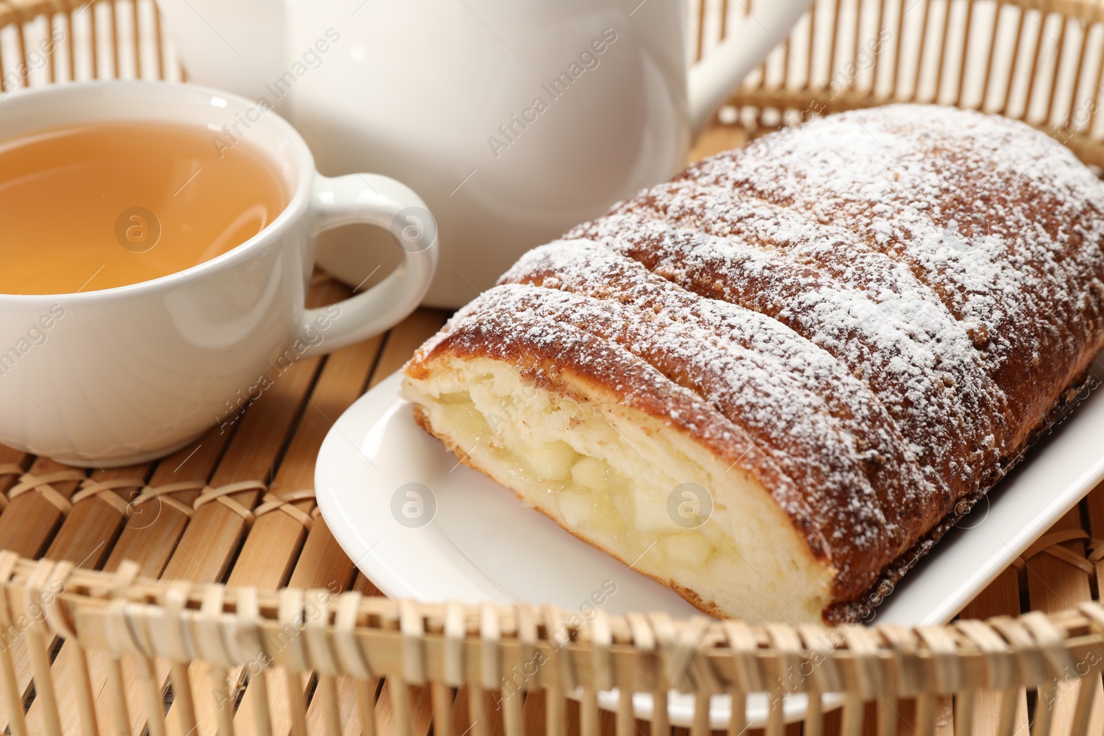 Photo of Delicious yeast dough cake and tea on wicker tray, closeup