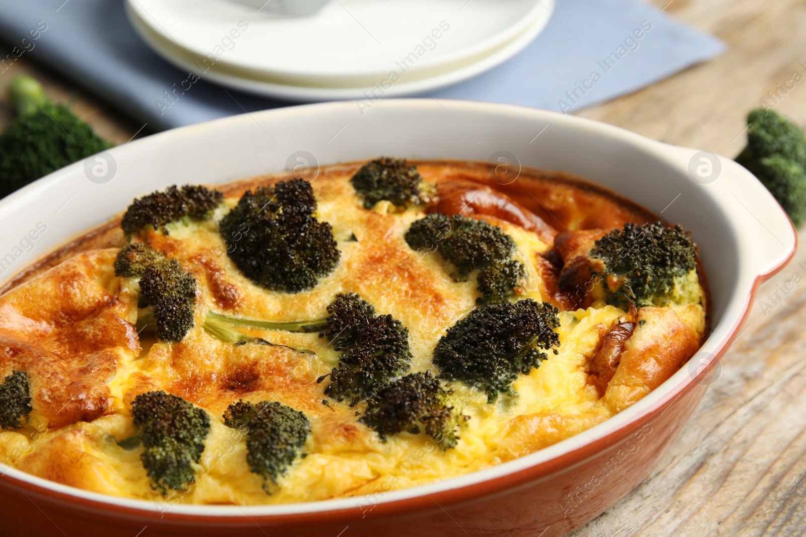 Photo of Tasty broccoli casserole in baking dish on wooden table, closeup