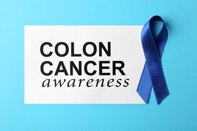 Photo of Paper with blue ribbon and text Colon cancer awareness on color background, top view
