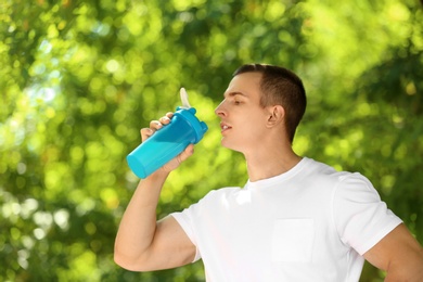 Athletic young man drinking protein shake at green park