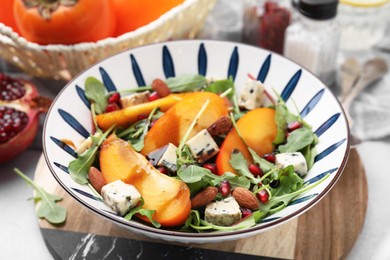 Photo of Tasty salad with persimmon, blue cheese, pomegranate and almonds served on white table, closeup