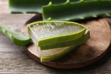 Photo of Slices of fresh aloe vera leaves with gel on wooden table, closeup