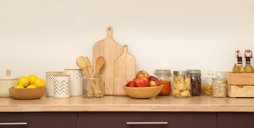 Photo of Wooden countertop with dishware and products near white wall. Kitchen interior idea