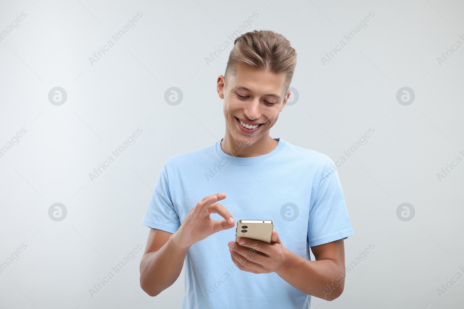 Photo of Happy young man sending message via smartphone on light grey background