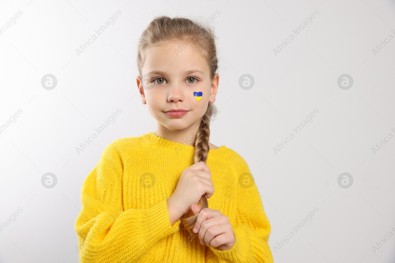 Photo of Little girl with drawing of Ukrainian flag on face against white background