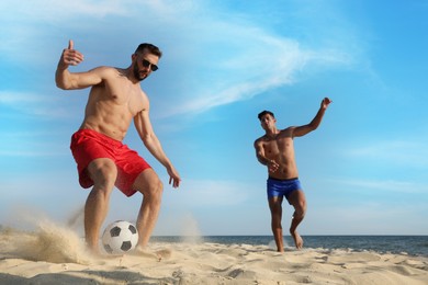 Friends playing football on sandy beach near sea