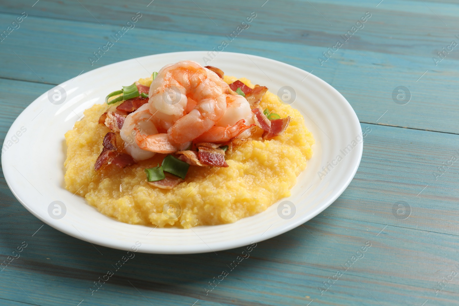 Photo of Plate with fresh tasty shrimps, bacon and grits on light blue wooden table