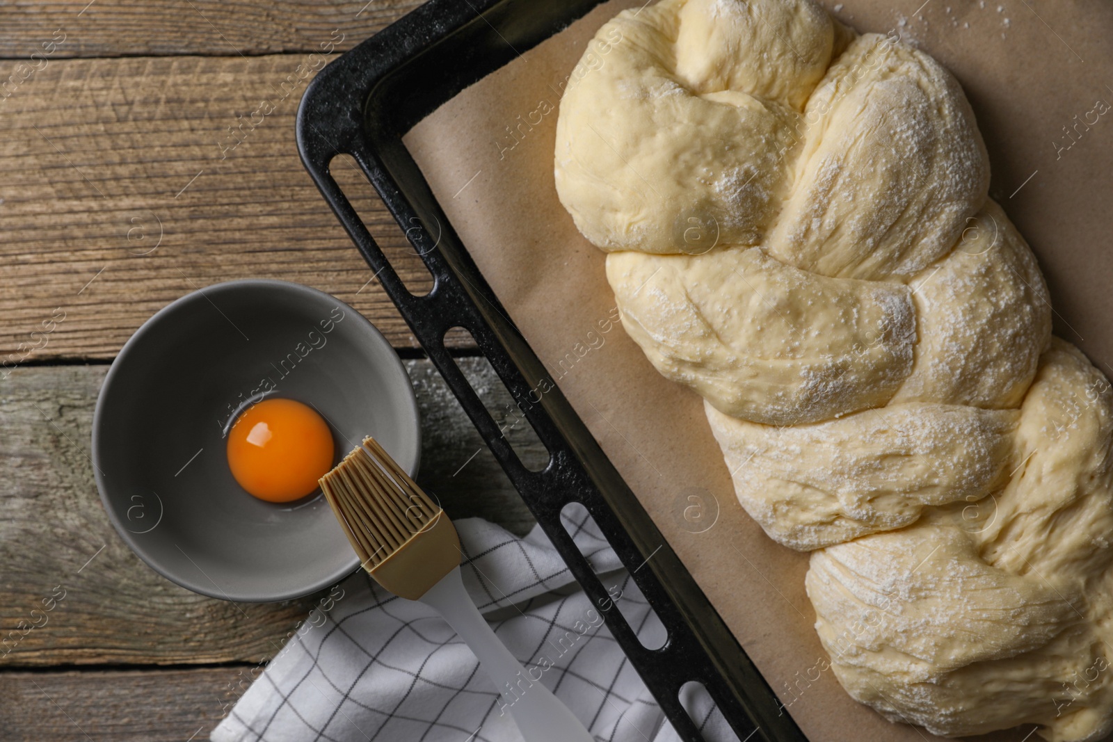 Photo of Homemade braided bread and ingredients on wooden table, flat lay. Cooking traditional Shabbat challah