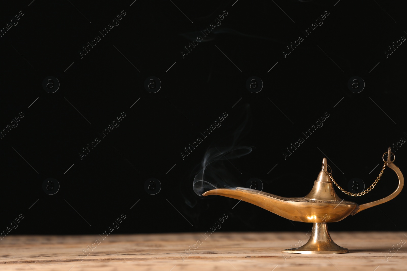 Photo of Aladdin lamp of wishes on wooden table against black background