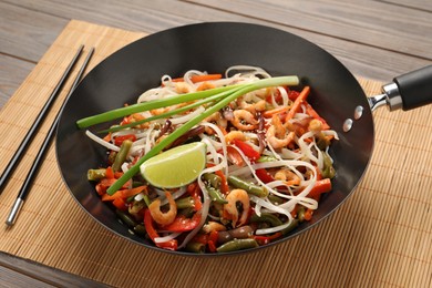 Photo of Shrimp stir fry with noodles and vegetables in wok on wooden table