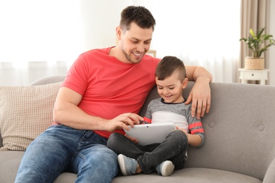 Photo of Boy and his father with tablet sitting on sofa at home. Family time