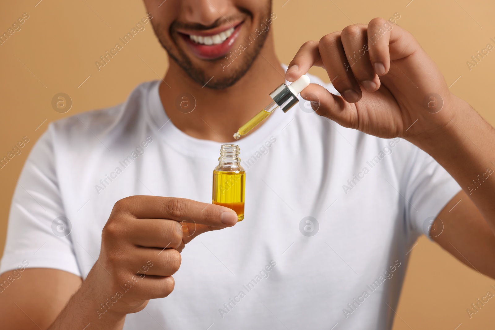 Photo of Man with cosmetic serum in hands on light brown background, closeup