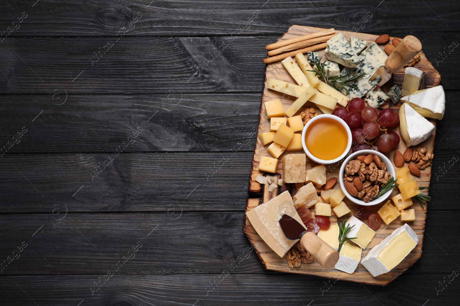 Photo of Cheese plate with honey, grapes and nuts on black wooden table, top view. Space for text