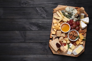 Photo of Cheese plate with honey, grapes and nuts on black wooden table, top view. Space for text