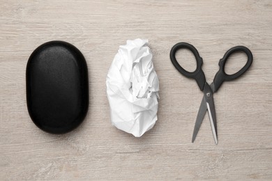 Photo of Rock, crumpled paper and scissors on wooden background, flat lay