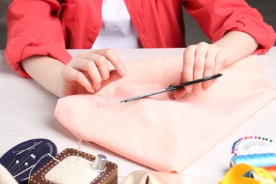 Woman cutting sewing thread over cloth at white wooden table, closeup