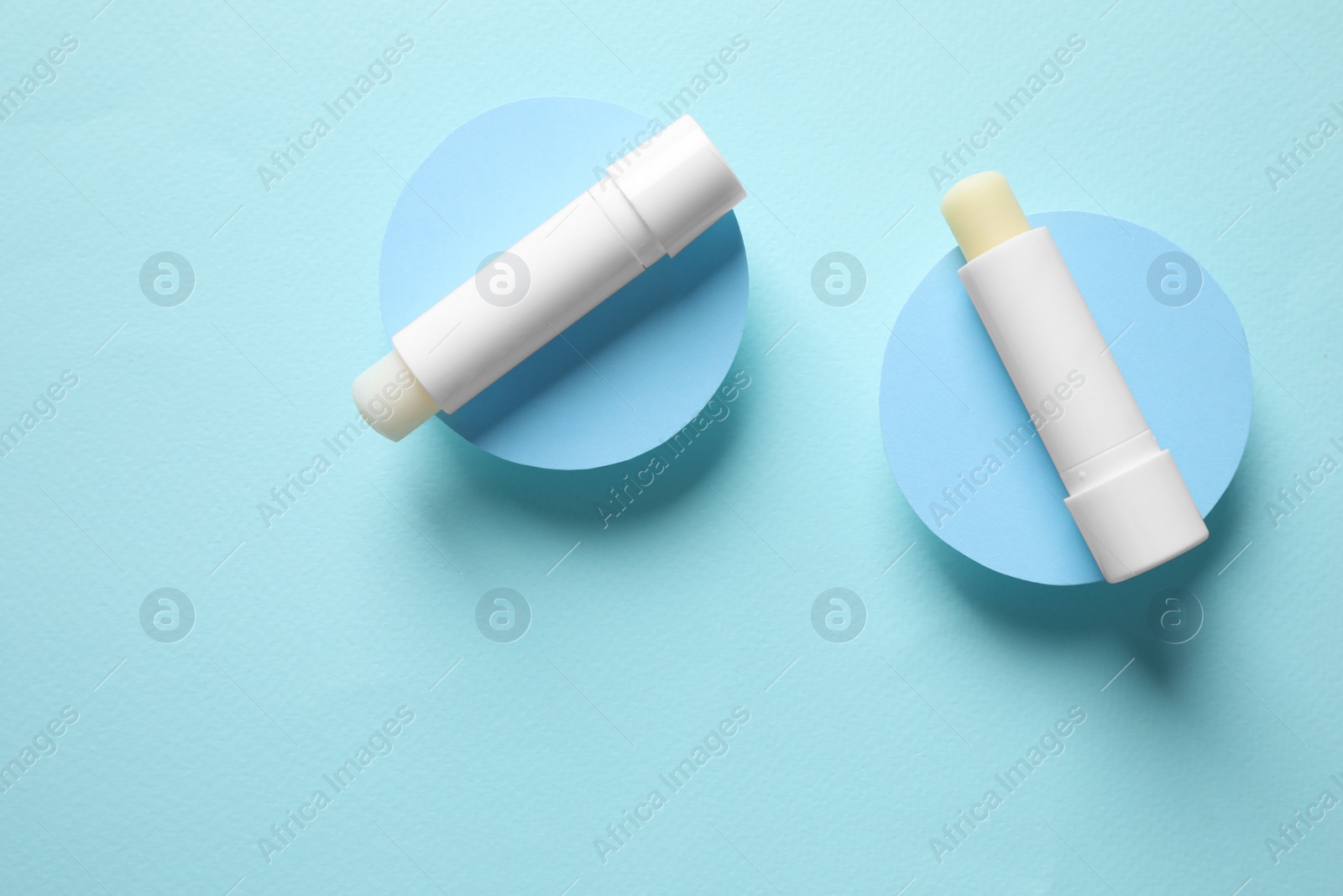 Photo of Hygienic lipsticks on turquoise background, flat lay