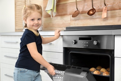 Photo of Little girl checking cookies in oven at home