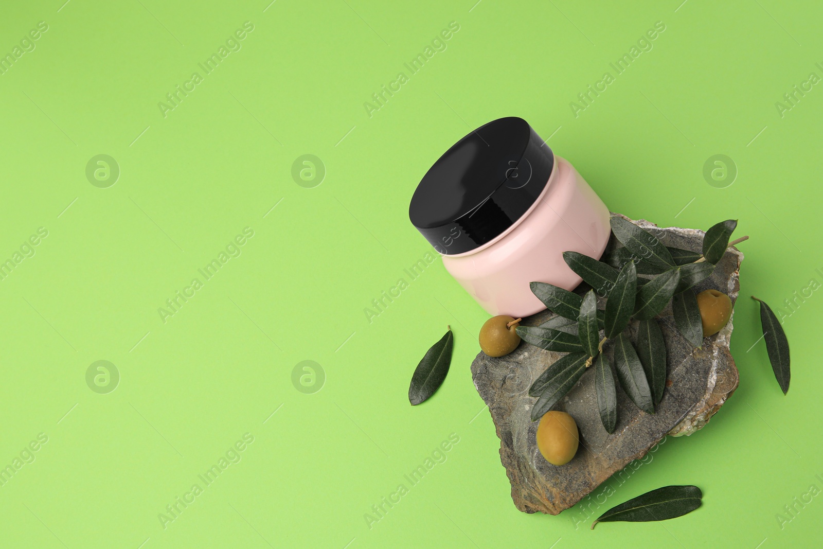 Photo of Jar of cream and olives on light green background, flat lay. Space for text