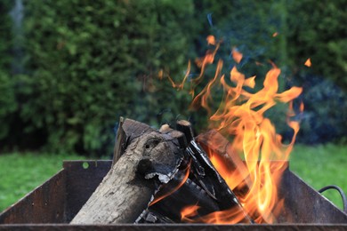 Photo of Metal brazier with burning firewood outdoors, closeup