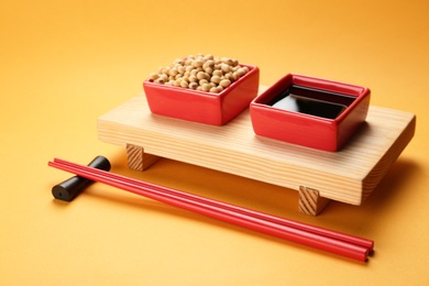 Photo of Bowls of soy sauce and beans on stand with chopsticks against color background