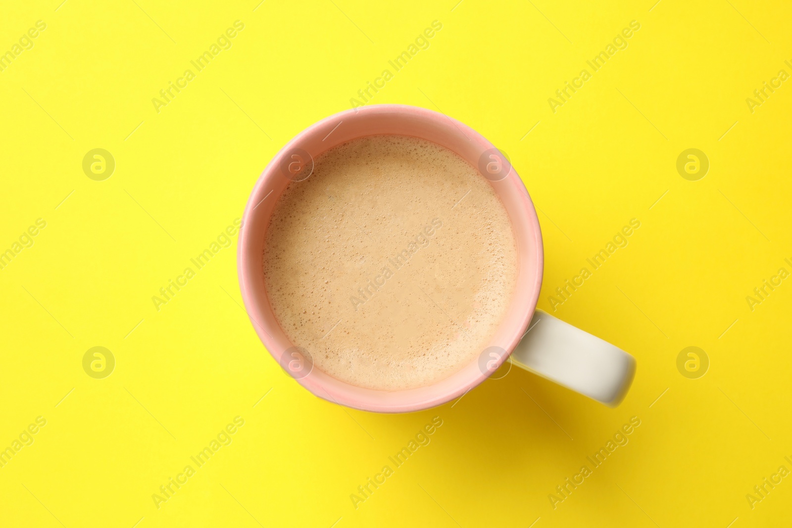 Photo of Aromatic coffee in cup on yellow background, top view