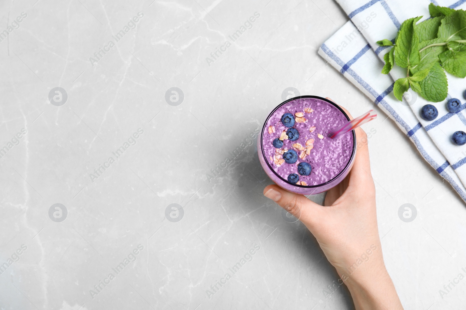 Photo of Woman holding glass of delicious blueberry smoothie on light marble table, top view. Space for text