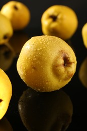Photo of Tasty ripe quinces with water drops on black mirror surface, closeup