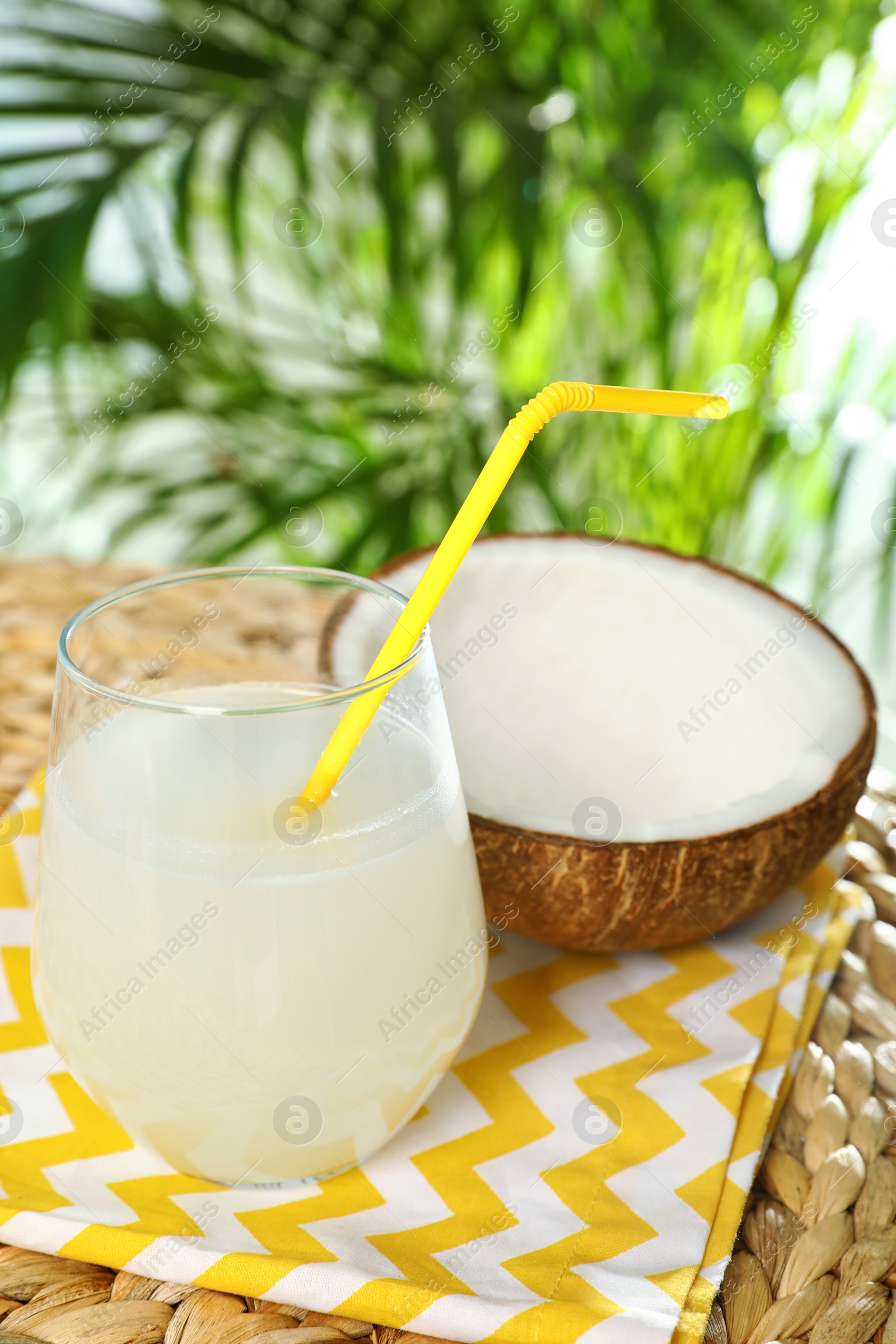 Photo of Composition with glass of coconut water on wicker table against blurred background