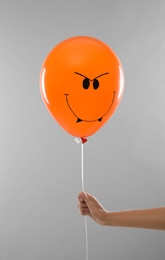 Photo of Woman holding spooky balloon for Halloween party on light grey background, closeup
