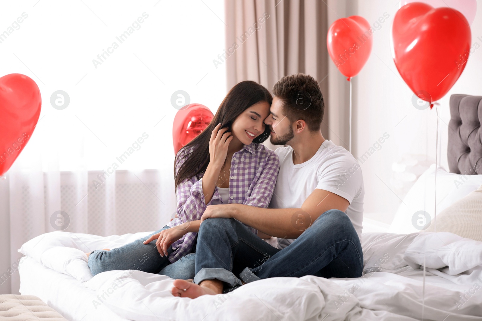 Photo of Lovely young couple in bedroom decorated with heart shaped balloons. Valentine's day celebration