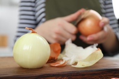 Photo of Woman peeling fresh onion with knife at table, focus on vegetable