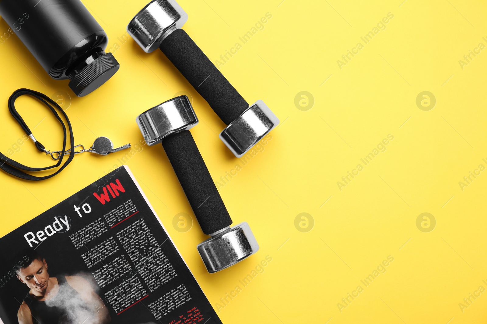 Photo of Metal dumbbells, whistle, magazine and plastic bottle on yellow background, flat lay. Space for text