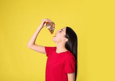 Beautiful woman eating tasty pizza on yellow background