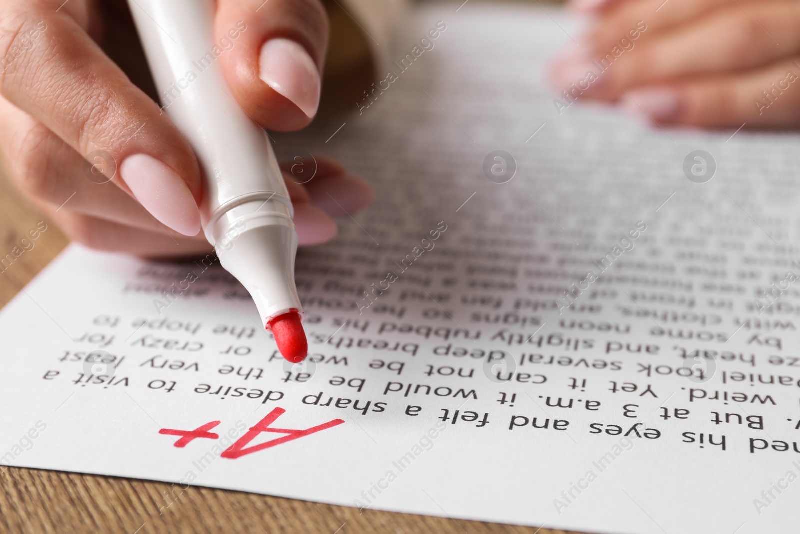 Photo of School grade. Teacher writing letter A with plus symbol on sheet of paper at wooden table, closeup