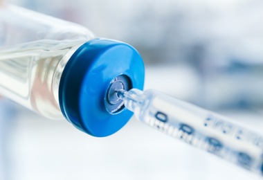 Photo of Vial with vaccine and syringe on blurred background