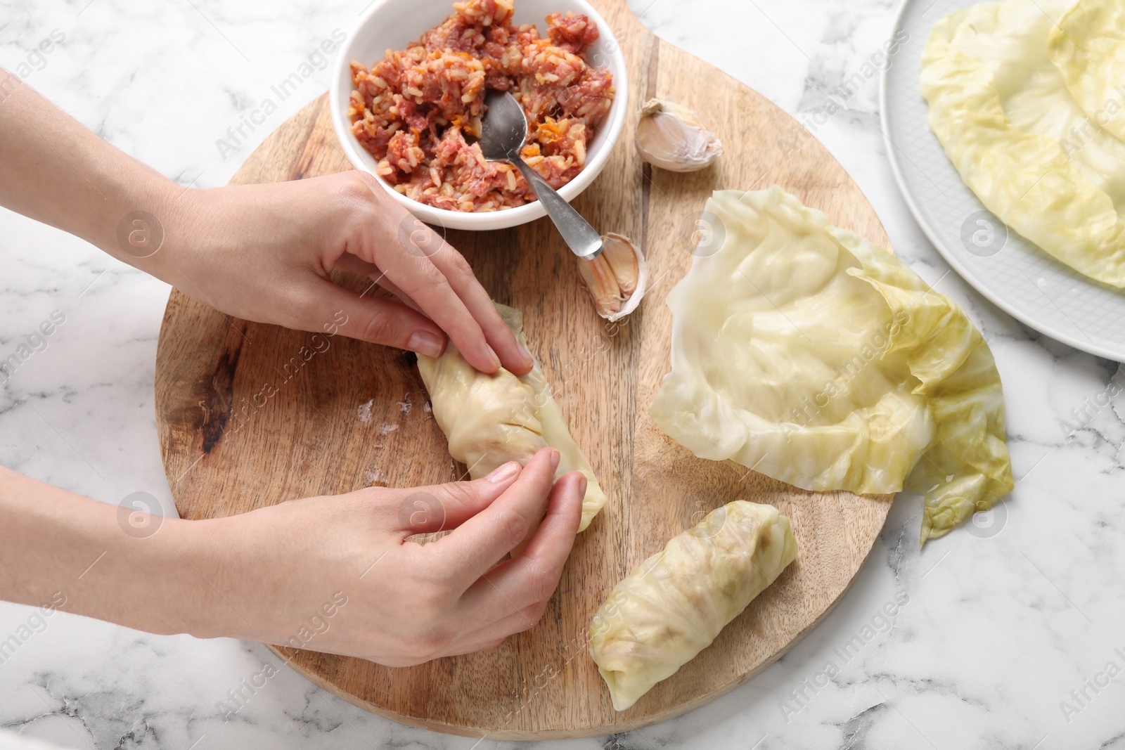 Photo of Woman preparing stuffed cabbage roll at white marble table, top view