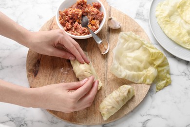 Photo of Woman preparing stuffed cabbage roll at white marble table, top view